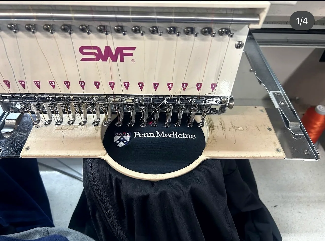 Commercial embroidery machine stitching a Penn Medicine logo on black apparel.